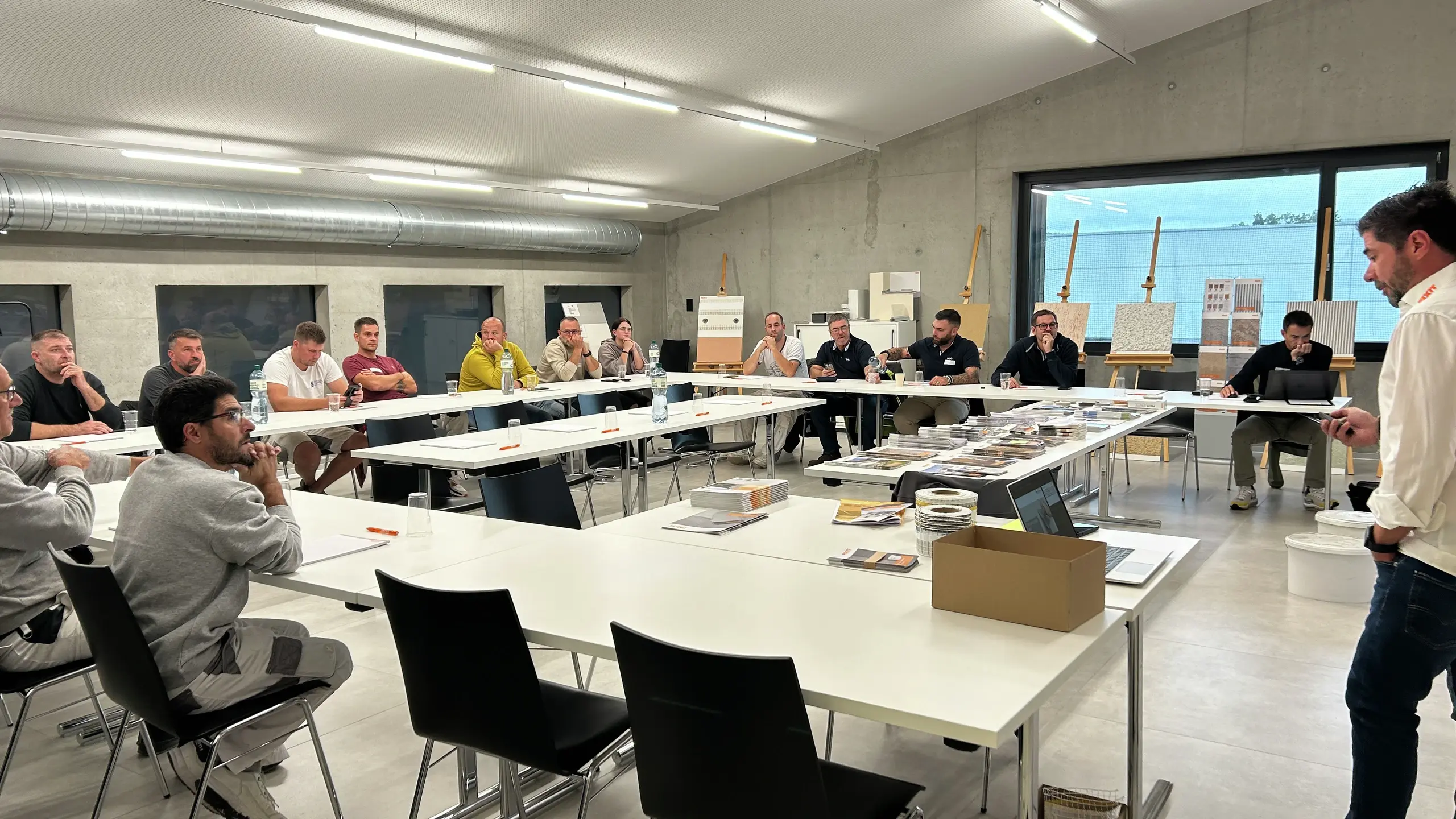 Les participants sont assis à des tables disposées en U et écoutent la conférence