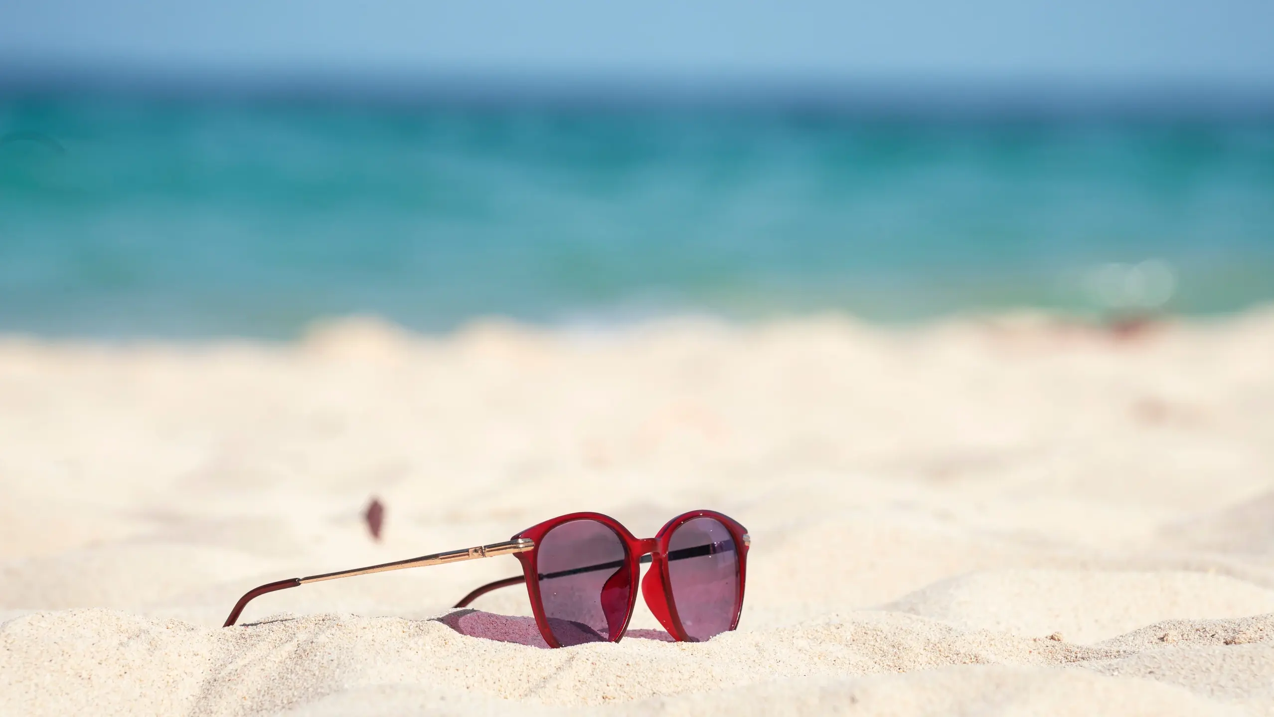 Rote Sonnenbrille liegt auf fast weissem Sand am Strand im Hintergrund türkises Meer
