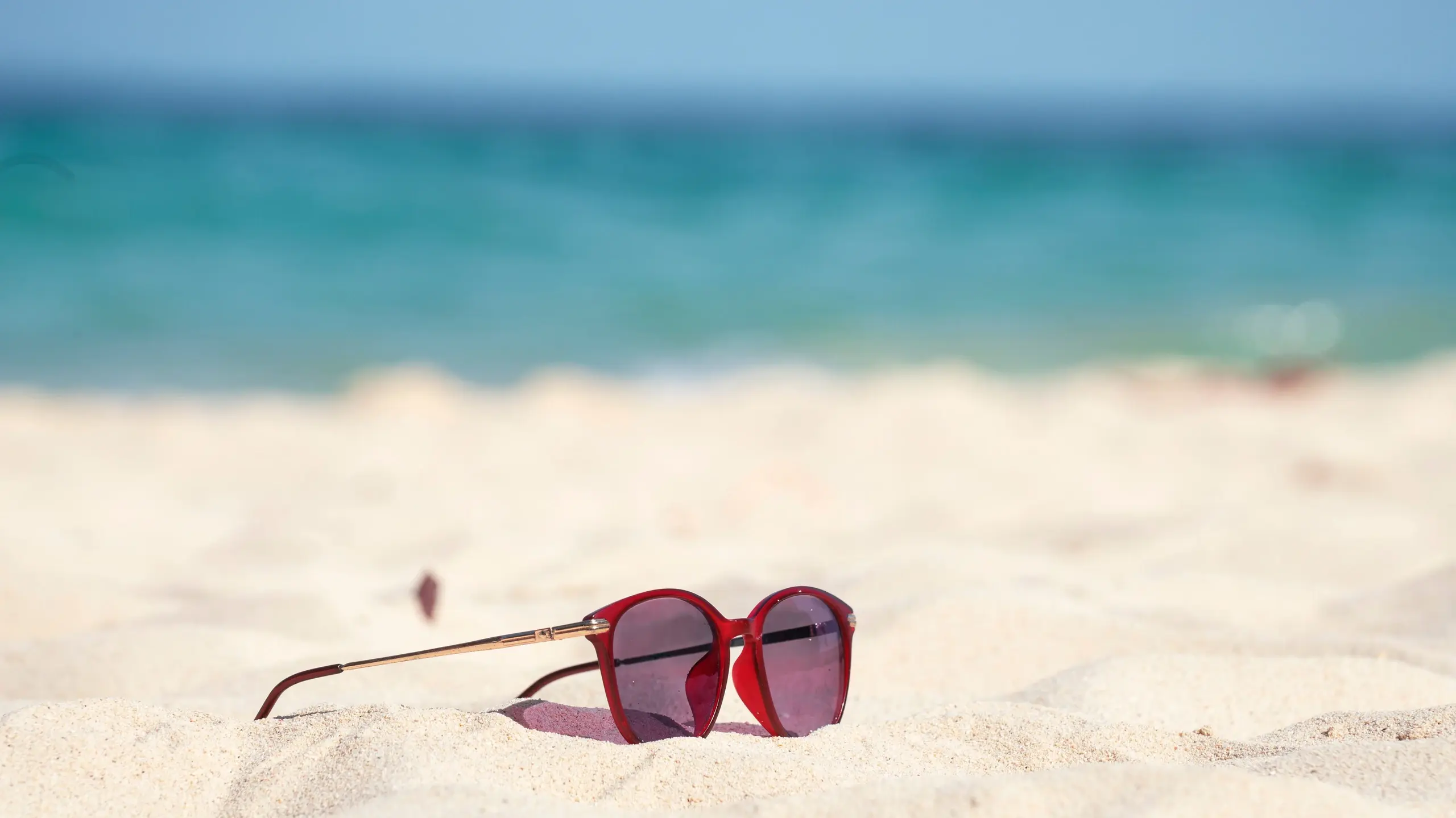 Rote Sonnenbrille liegt auf fast weissem Sand am Strand im Hintergrund türkises Meer