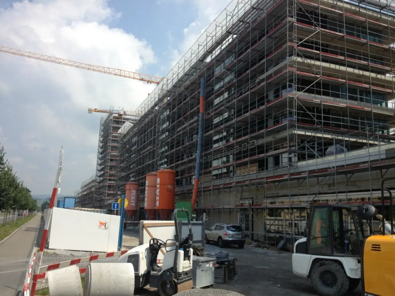 Eingerüstete Gebäude mit mehreren orangenen Fixit Silos und Baustellenequipment