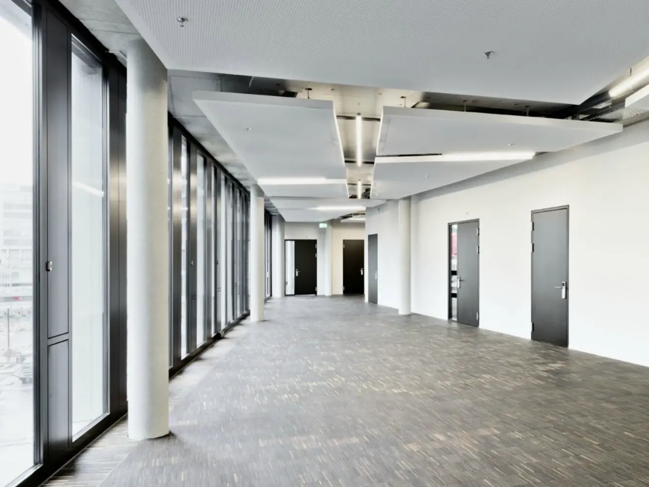 Flur im Gebäude mit Verglasung links und abgehenden Türen rechts.