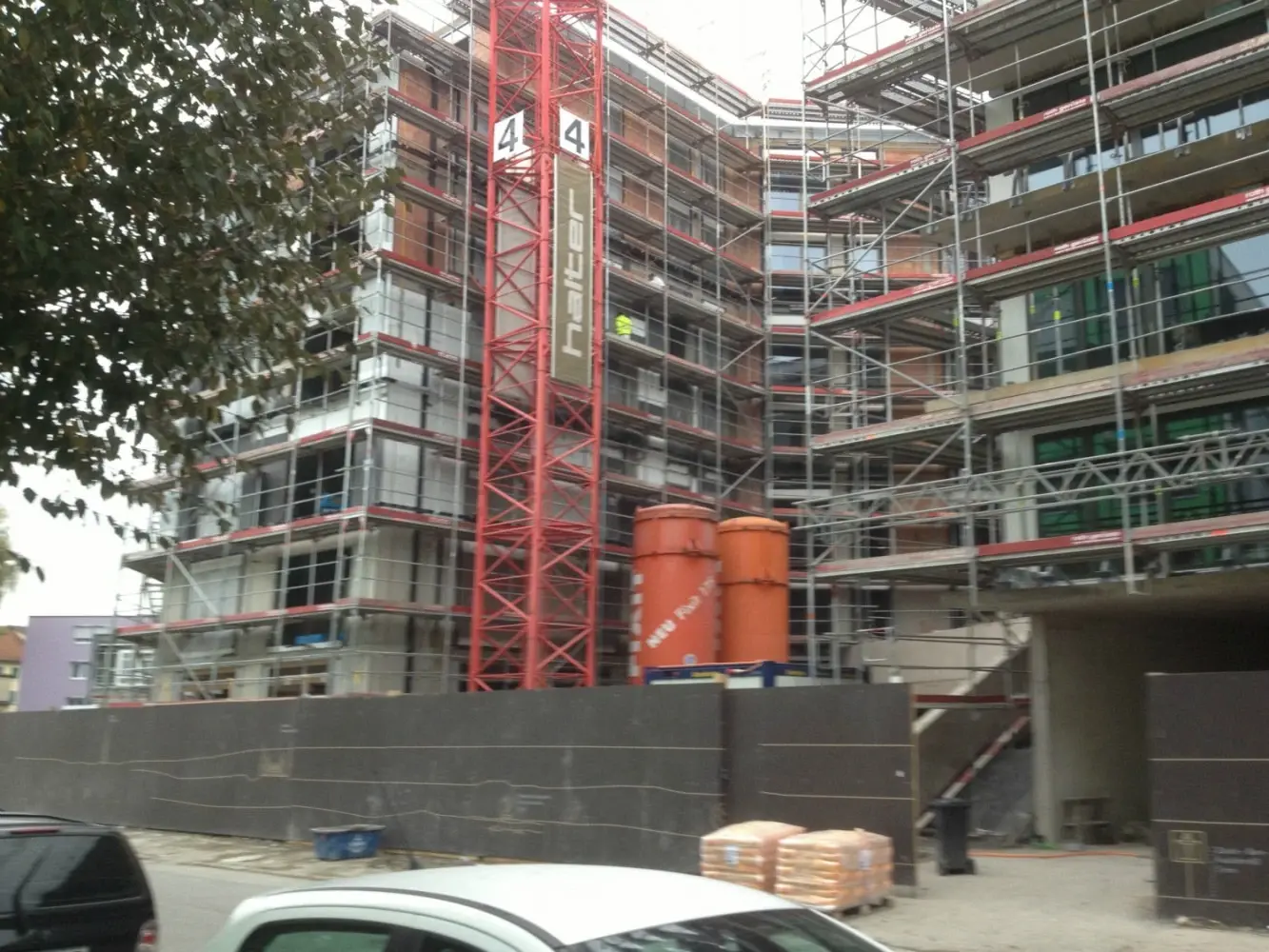 Eingerüstetes Gebäude mit zwei orangenen Fixit Silos und rotem Kran