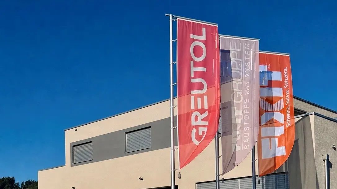 Drei Fahnen in rot mit Greutol Schriftzug, Grau mit Fixit Gruppe Schriftzug und orange mit Fixit Schriftzug vor dem Fixit Gebäude in Wilen
