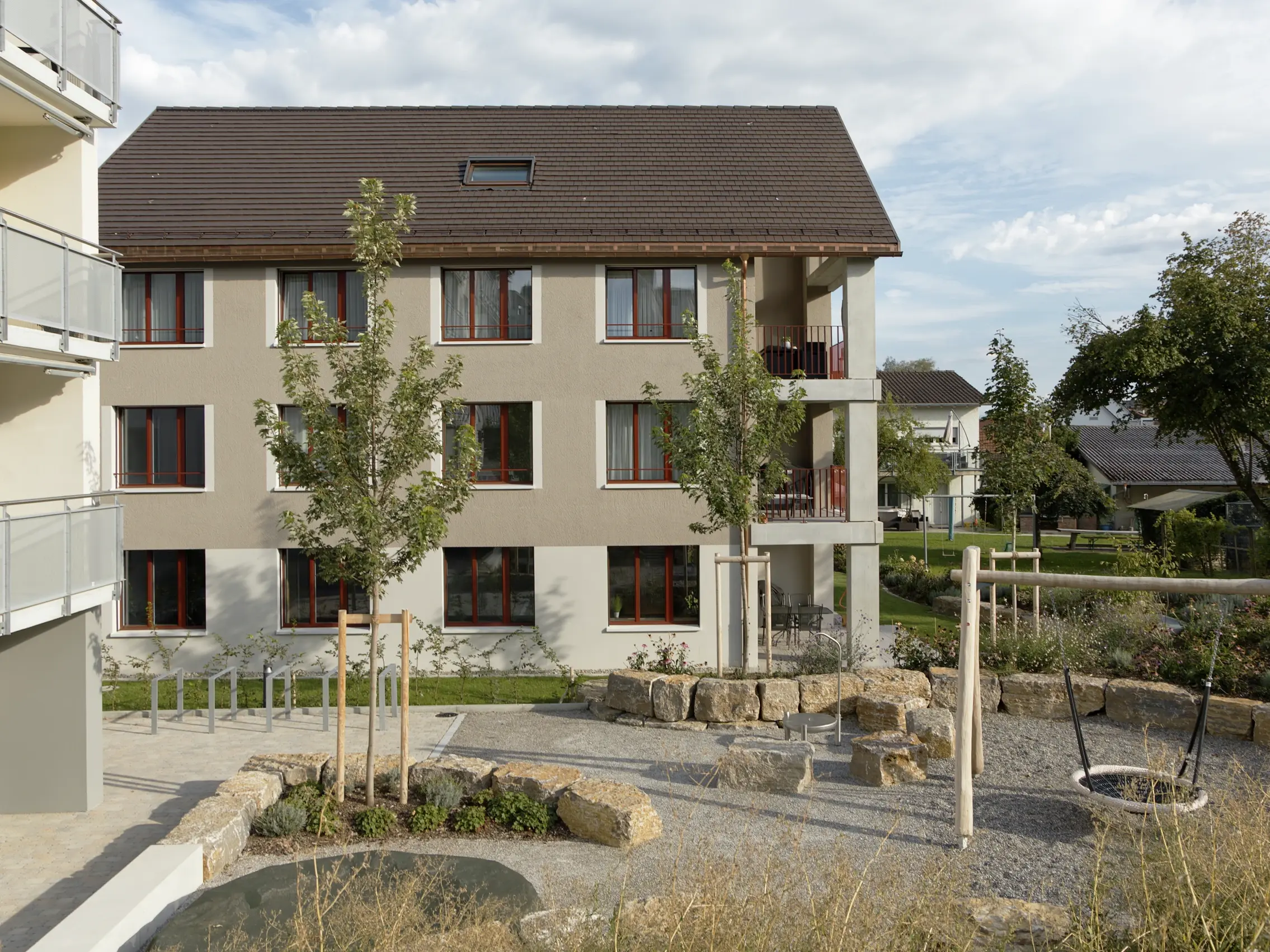 Vue de l'arrière du bâtiment avec aire de jeux, balançoire et espaces verts