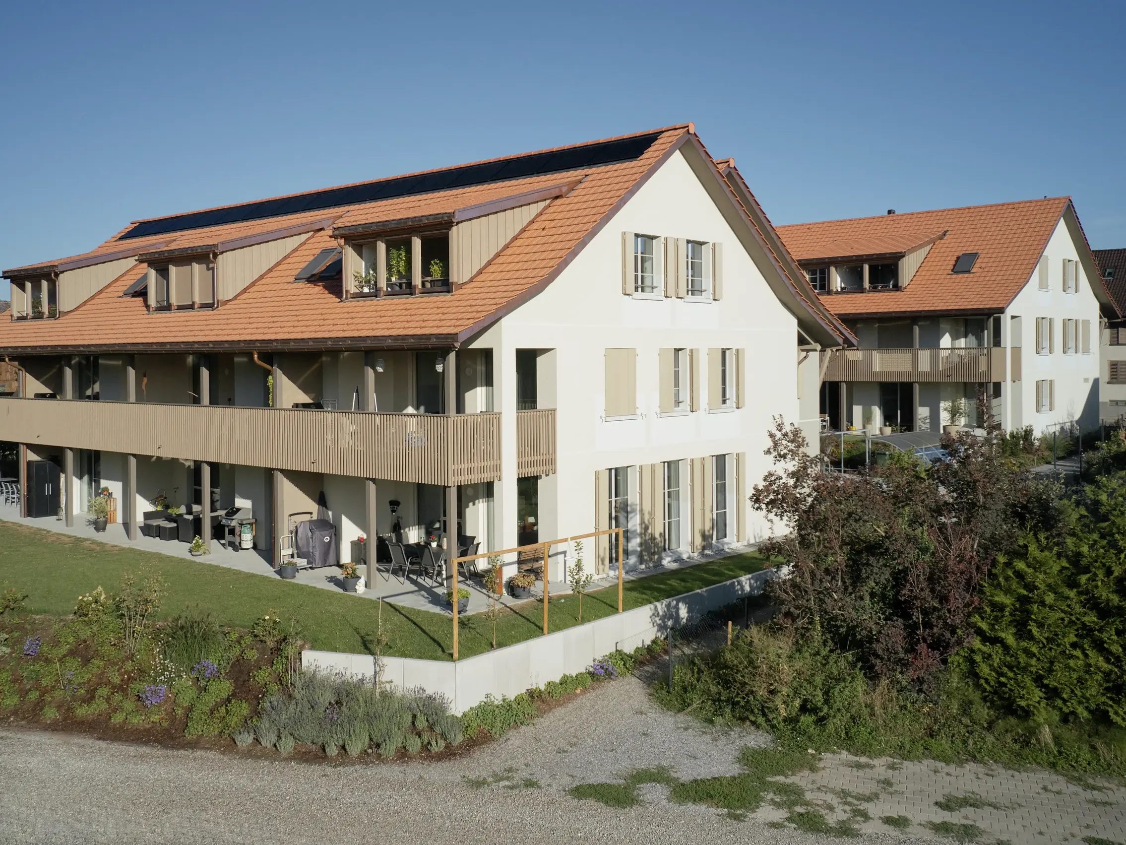 Ansicht der beiden Gebäude mit weiss verputzter Aussenfassade bei Sonnenschein und blauem Himmel