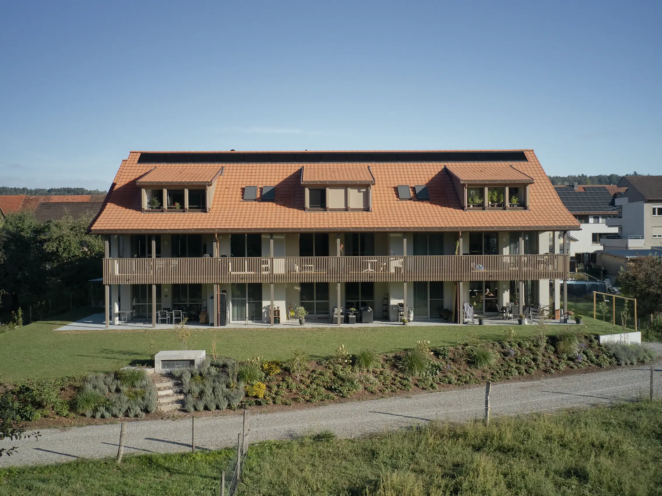 Ansicht der Gebäuderückseite mit Garten, den drei Dachgauben und dem durchlaufenden Balkongeländer