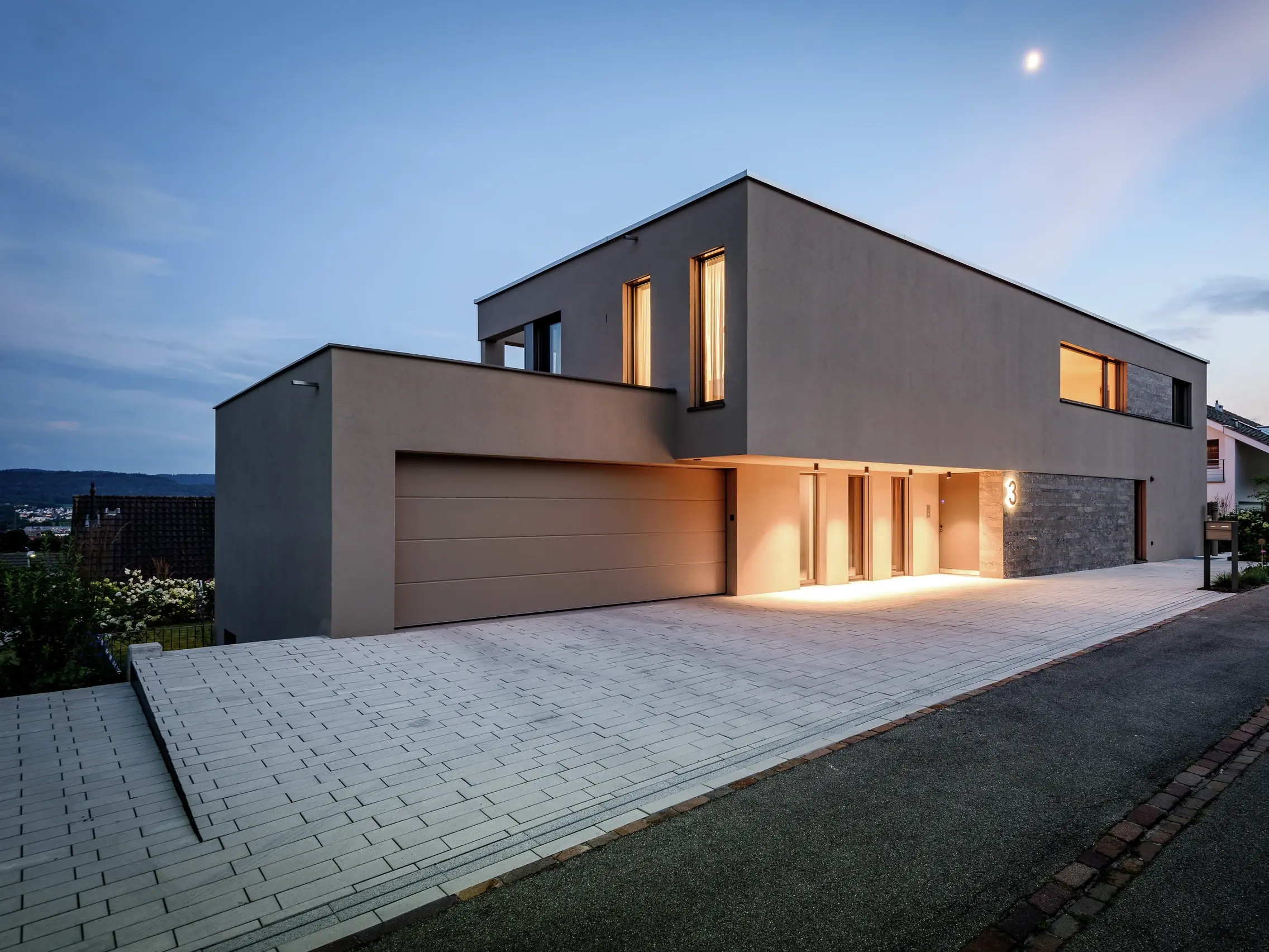 Ansicht von der Strassenseite, gepflasterte Hofeinfahrt mit Garage und Beleuchtung