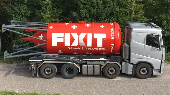 Grauer Lastwagen mit rotem Fixit Silo mit Schweizer Kreuzen auf der Ladefläche vor einem Wald