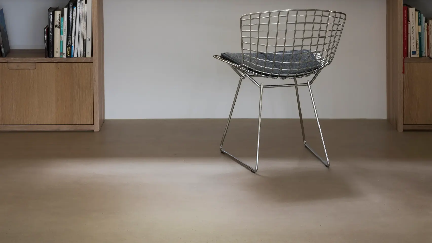 Chaise design en métal posée sur le sol en chape apparente de couleur crème d'un salon