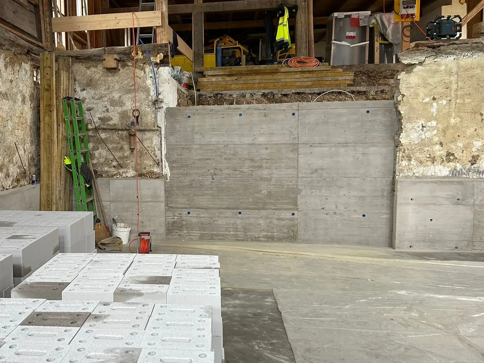 L'ouverture murale bouchée par un mur en béton, avec des palettes remplies de pierres au premier plan
