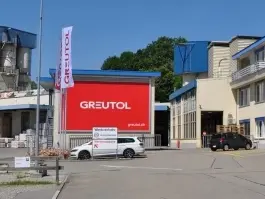 Ansicht des Greutol Standorts in Otelfingen mit grossem Greutol Logo auf dem blau-beigen Gebäude