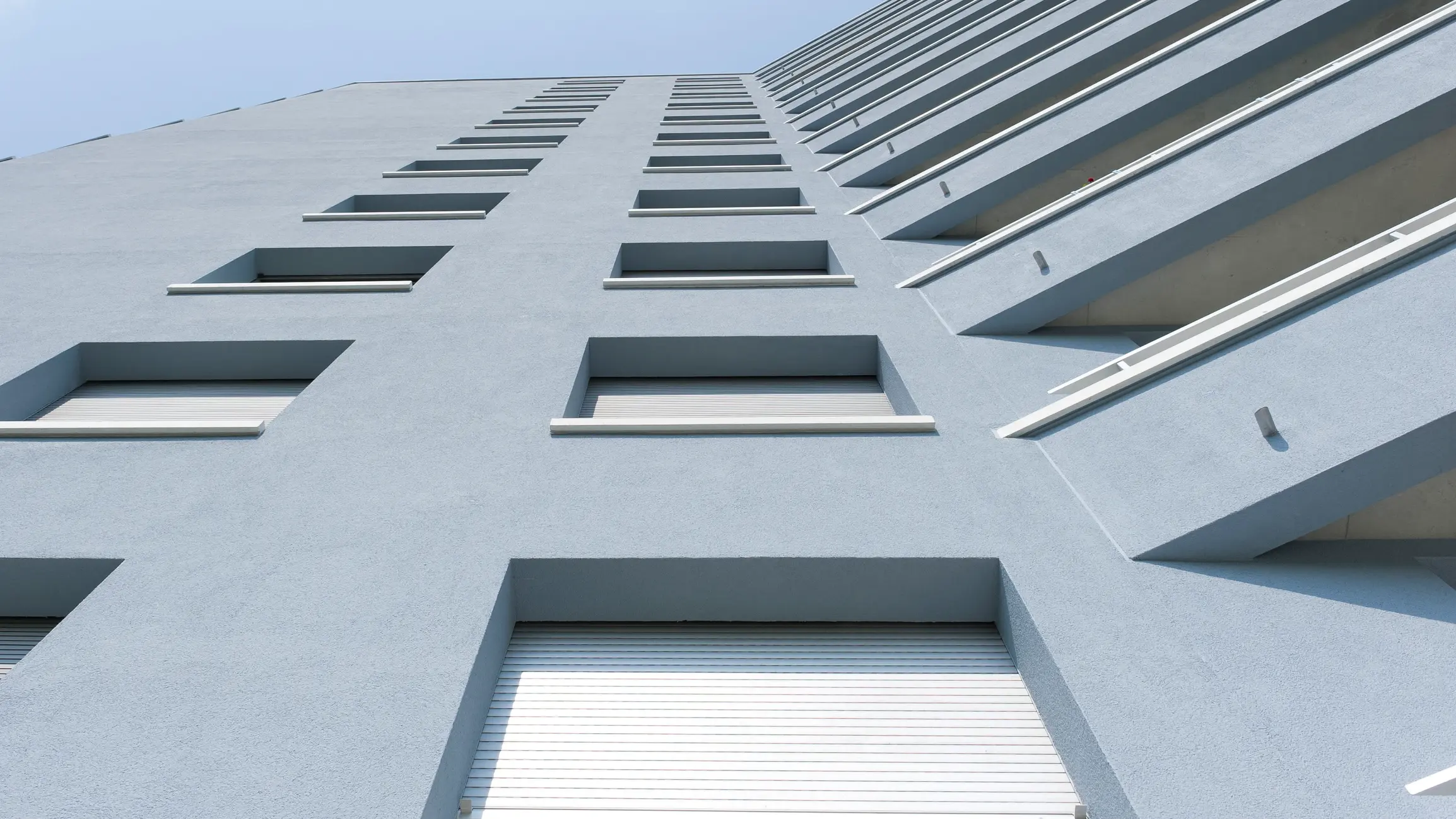 Vue du bas vers le haut sur la façade crépie bleu pigeon d'un immeuble résidentiel de plusieurs étages