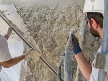 Verarbeiter spritzen Aerogel Hochleistungsdämmputz auf eine Wand und ziehen den Putz mit der Latte ab