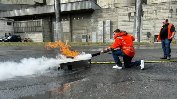 Ein Mitarbeiter löscht den Testbrand mit einem Feuerlöscher unter Aufsicht des Lehrers