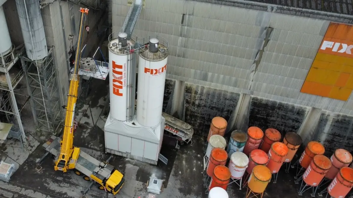 Drohnenaufnahme von der grossen Werkshalle in Holderbank, gelber Kran zwischen den Fixit Silotürmen und kleinen, orangenen Silos