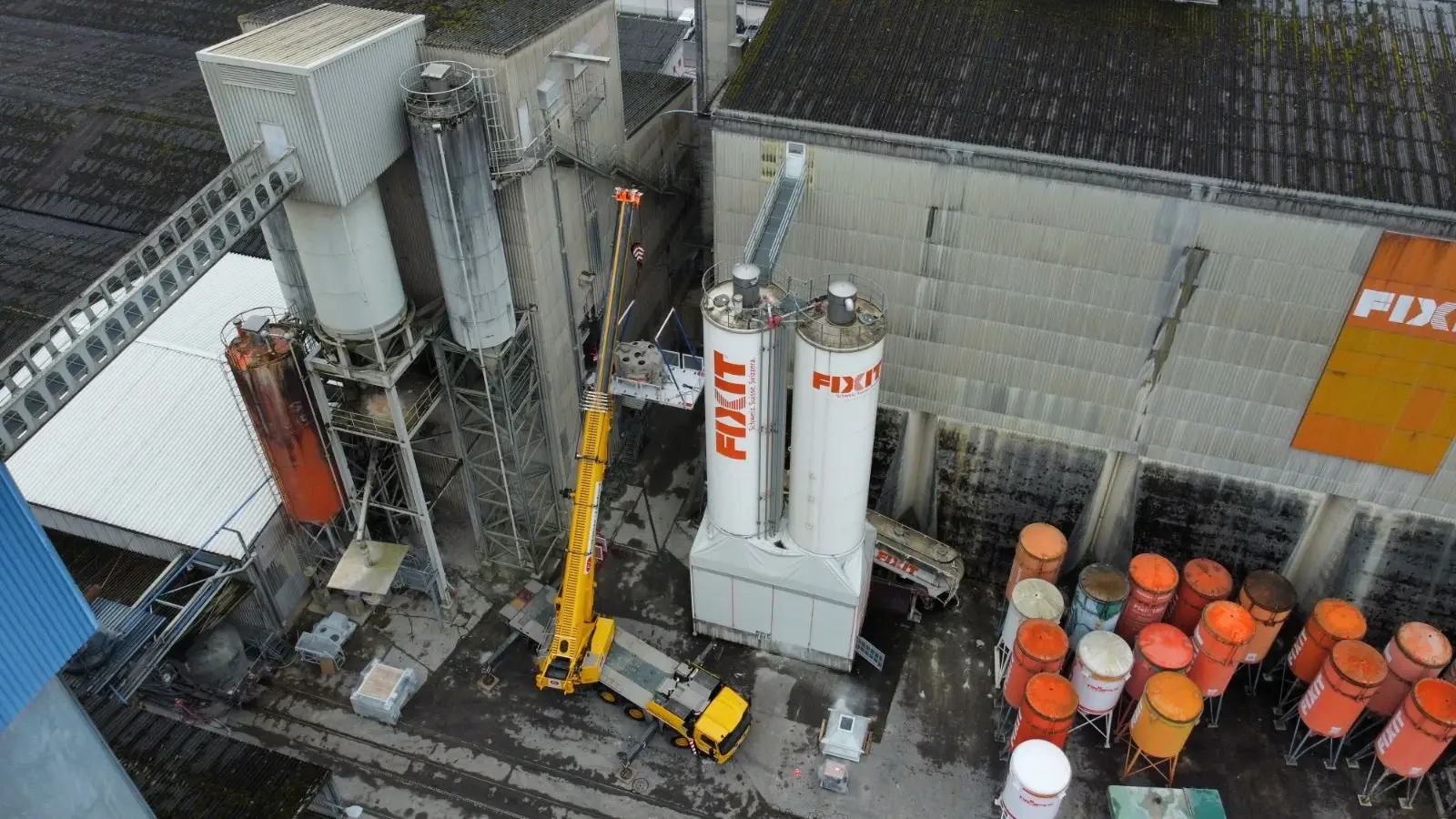 Drohnenaufnahme von der grossen Werkshalle in Holderbank, gelber Kran zwischen den Fixit Silotürmen und kleinen, orangenen Silos