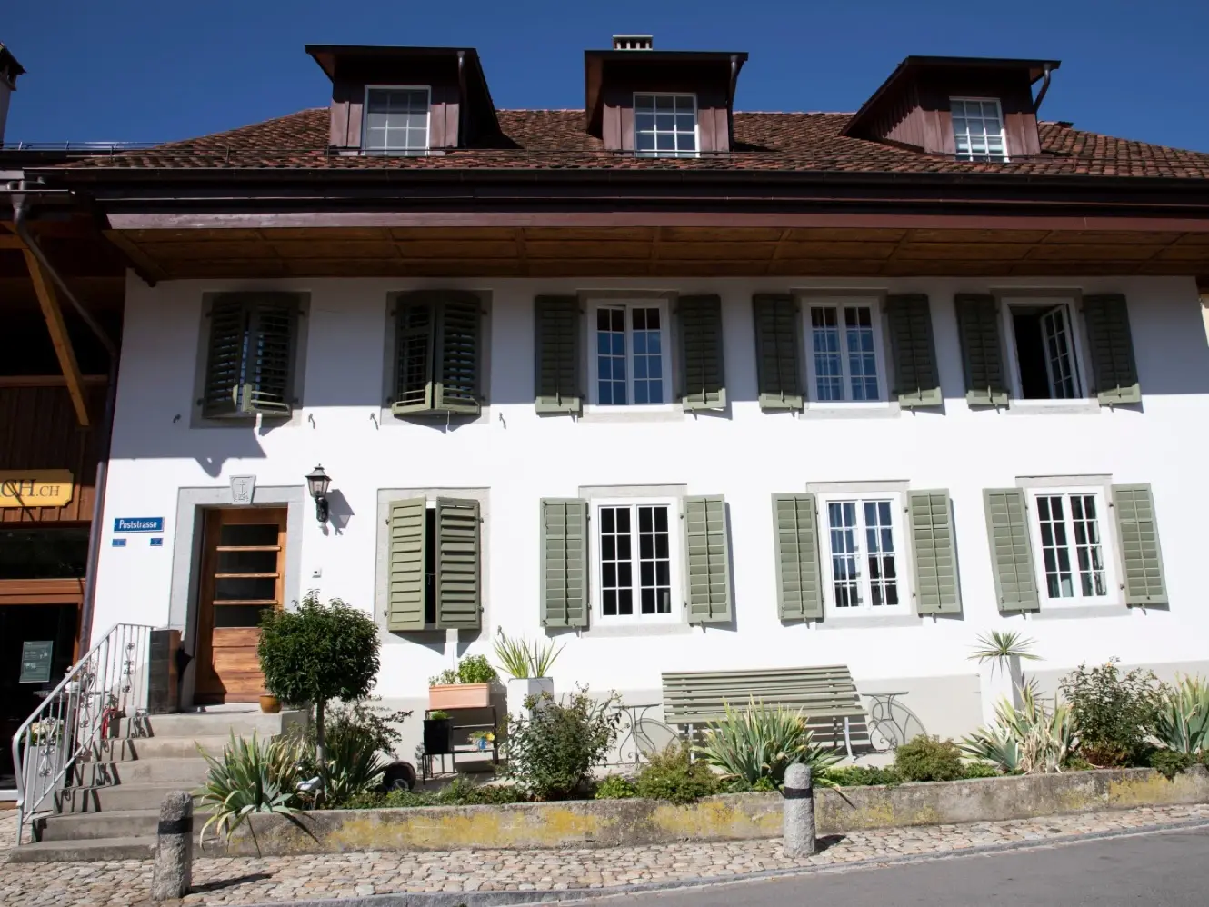 Frontansicht des weiss verputzten Gebäudes mit grünen Fensterläden von der Strasse aus