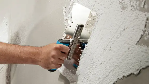 Mit einer Kelle wird eine Schicht Putz auf die Wand aufgetragen.
