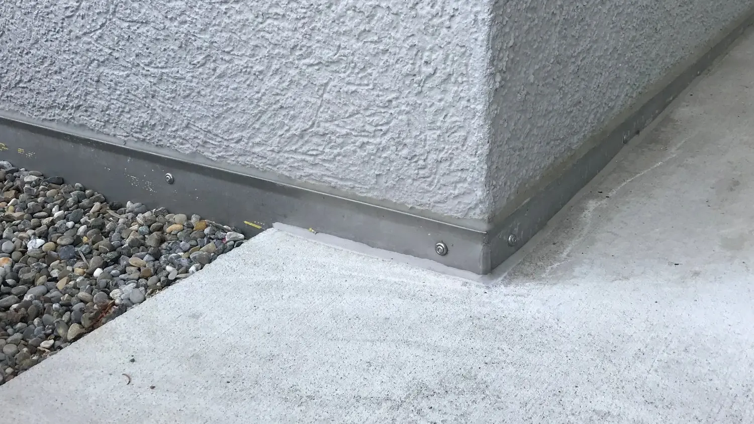 Coin de socle avec finition en tôle étroite et crépi blanc sur dalle en béton