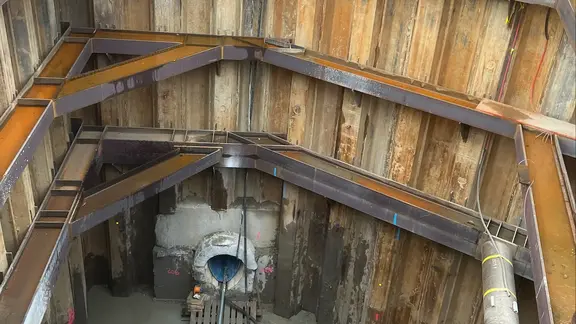 Sicht von oben in die gesicherte Baugrube mit dem Kanalausgang und Inliner am unteren Bildrand