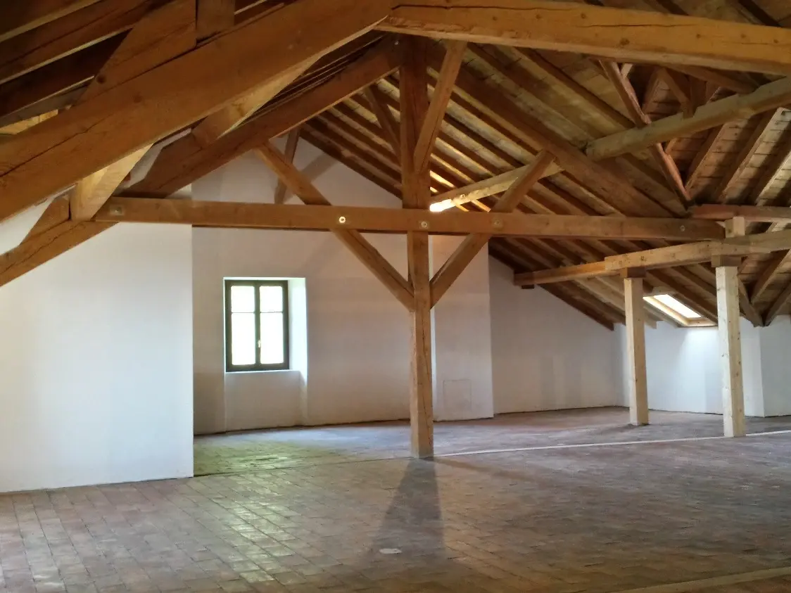 Dachgeschoss im Innenraum mit freiliegenden Balken, weiss verpputzten Wänden und schönen Boden