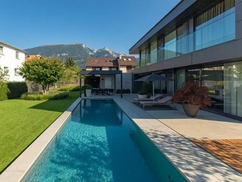 la piscine dans toute sa longueur, avec une prairie verdoyante à gauche et le bâtiment d'habitation à droite