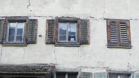 Façade extérieure délabrée avec des fissures horizontales profondes au-dessus des fenêtres et des fissures verticales le long des fenêtres