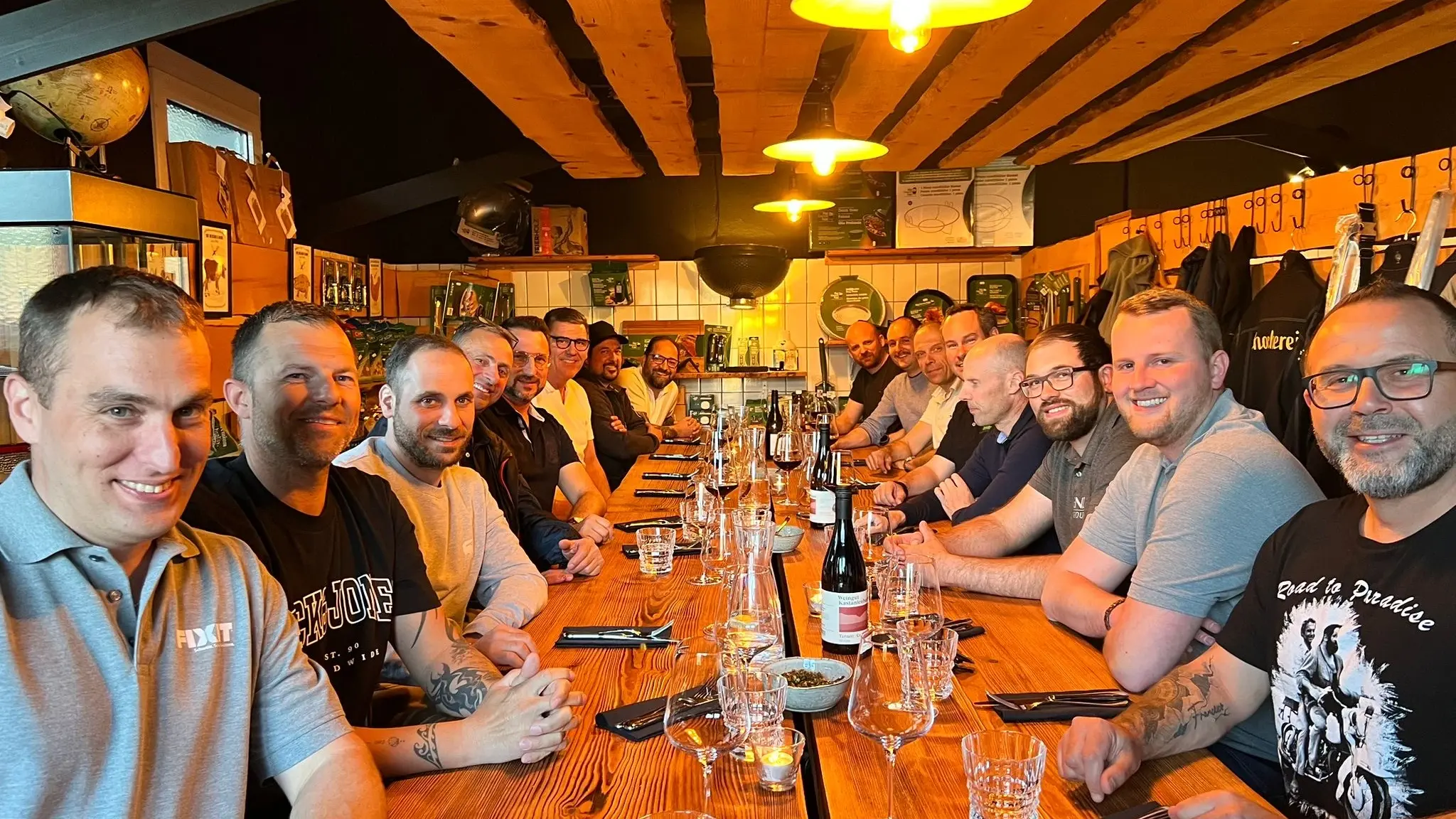 Gruppenfoto von Fixit Aussendienstmitarbeitern und Kunden an einem langen, rustikalen Holztisch und gelber Beleuchtung