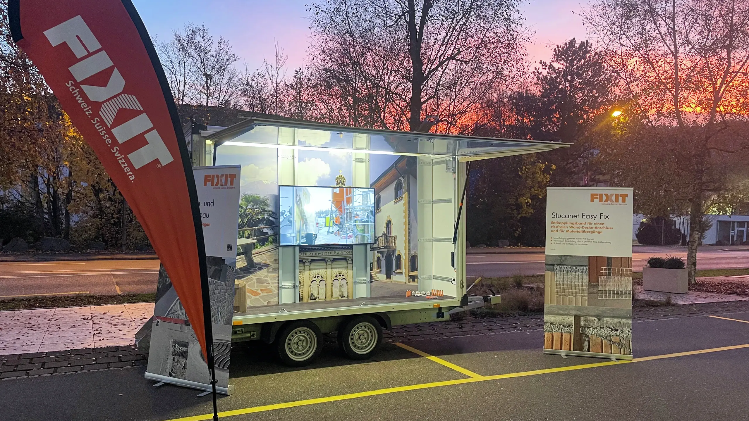 Fixit Beach Flag vor dem beleuchteten Fixit Roadshowanhänger im Sonnenaufgang