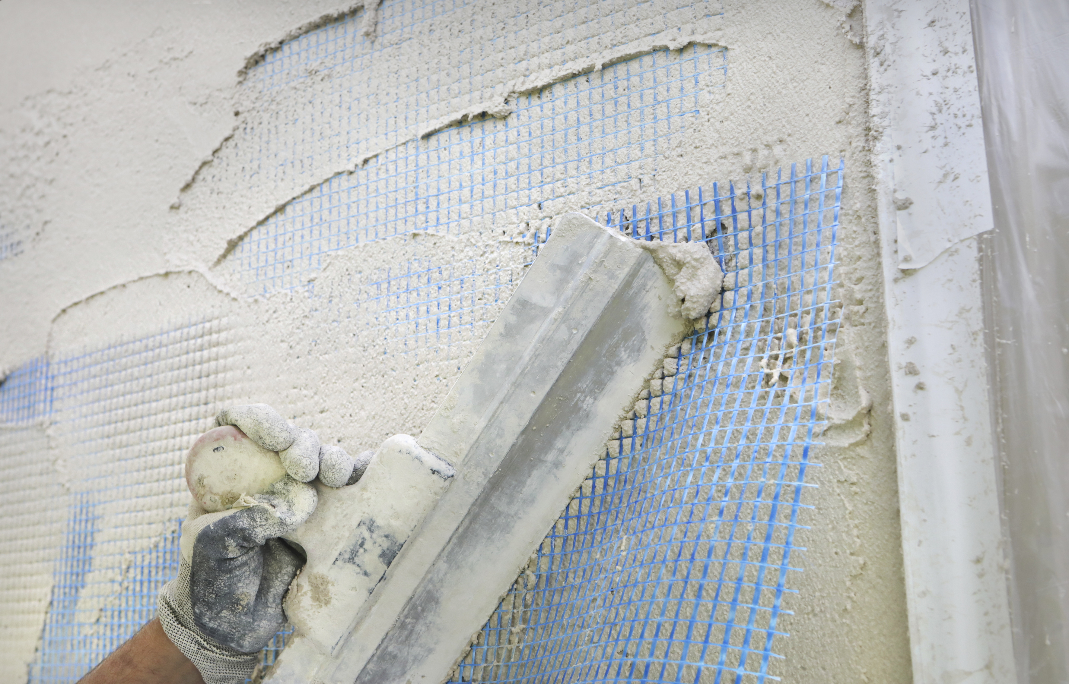 Eine Hand verputzt mit einem Spachtel eine Wand.