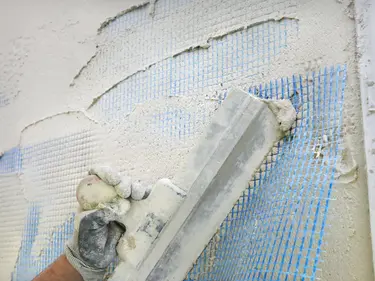 Eine Hand verputzt mit einem Spachtel eine Wand.