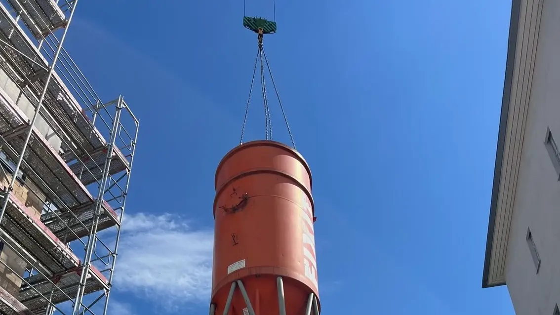 Silo Fixit orange suspendu en l'air à une grue et flottant à côté du bâtiment avec échafaudage
