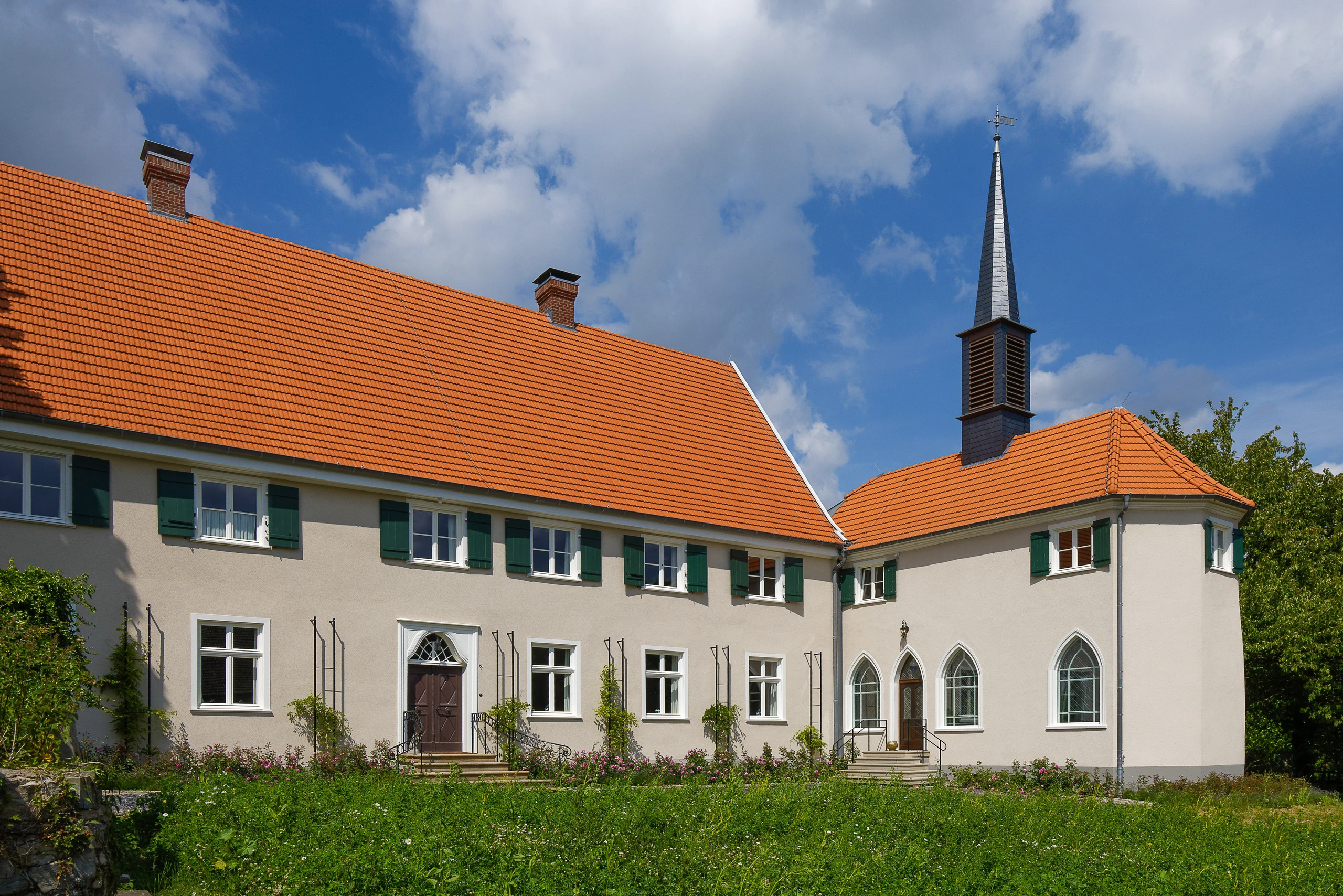 Historischer Gebäudekomplex mit beiger Aussenfassade und einem Gutshaus auf der linken Seite sowie einer angeschlossenen Kapelle mit spitzem Turm auf der rechten Seite