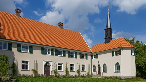 Historischer Gebäudekomplex mit beiger Aussenfassade und einem Gutshaus auf der linken Seite sowie einer angeschlossenen Kapelle mit spitzem Turm auf der rechten Seite