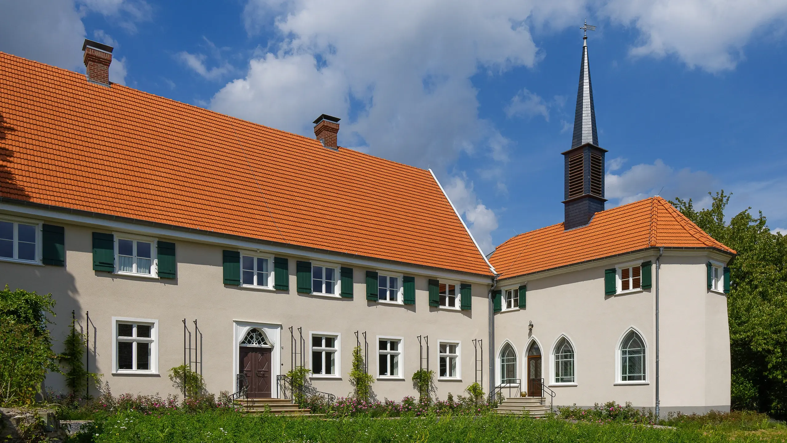 Historischer Gebäudekomplex mit beiger Aussenfassade und einem Gutshaus auf der linken Seite sowie einer angeschlossenen Kapelle mit spitzem Turm auf der rechten Seite