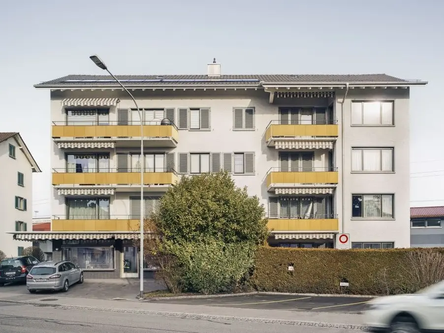 Gesamtansicht des Gebäudes mit einem fahrenden Auto und einem parkenden Auto