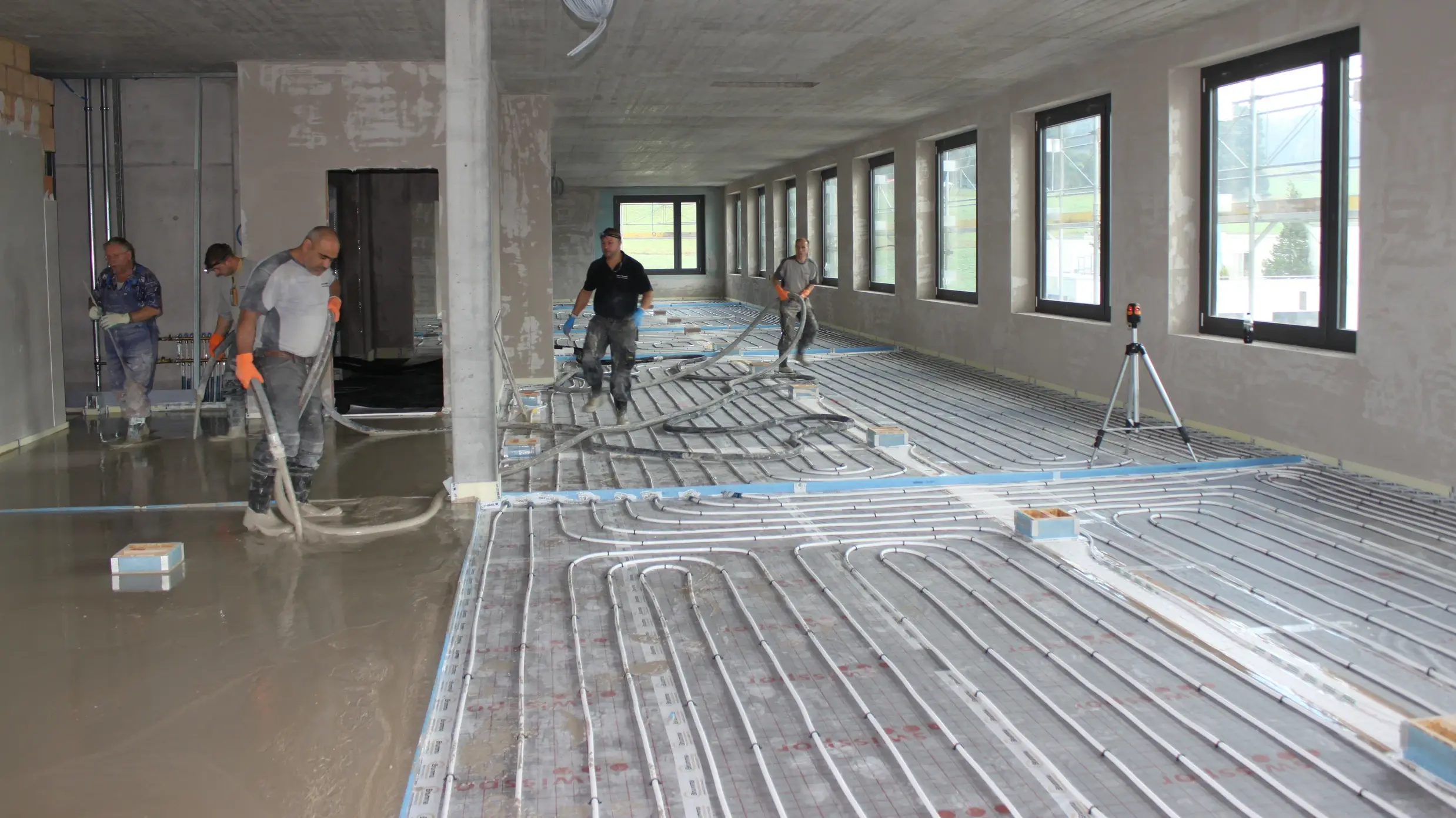  Chantier à l'intérieur avec des registres de chauffage posés pour le chauffage au sol. Sur la gauche, la chape fluide a déjà été coulée.
