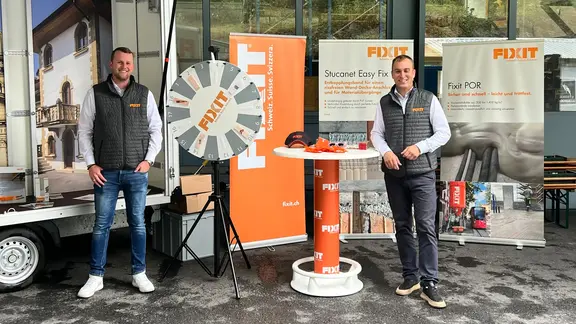 Fixit Mitarbeiter Thierry Lips (links) und Miroslav Rousar (rechts) vor dem Roadshow-Anhänger mit Fixit Glücksrad, Stehtisch und drei Werbebannern