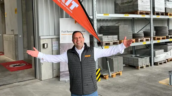 Notre collaborateur du service extérieur Fixit accueille aimablement tous les clients à bras ouverts lors de notre manifestation, un drapeau de plage avec le logo Fixit en arrière-plan.