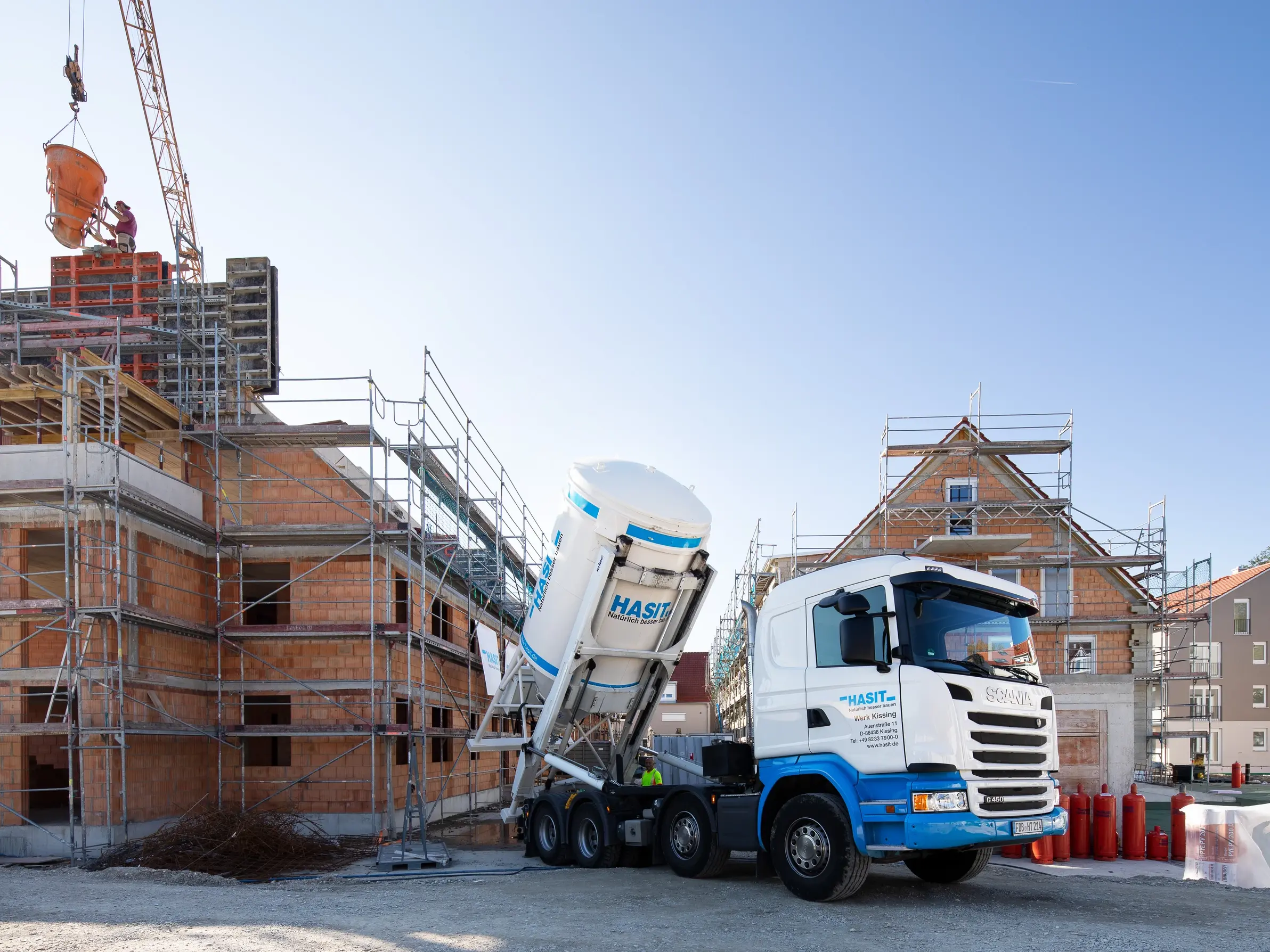 Un camion blanc et bleu décharge un silo blanc de la marque Hasit devant un bâtiment en construction