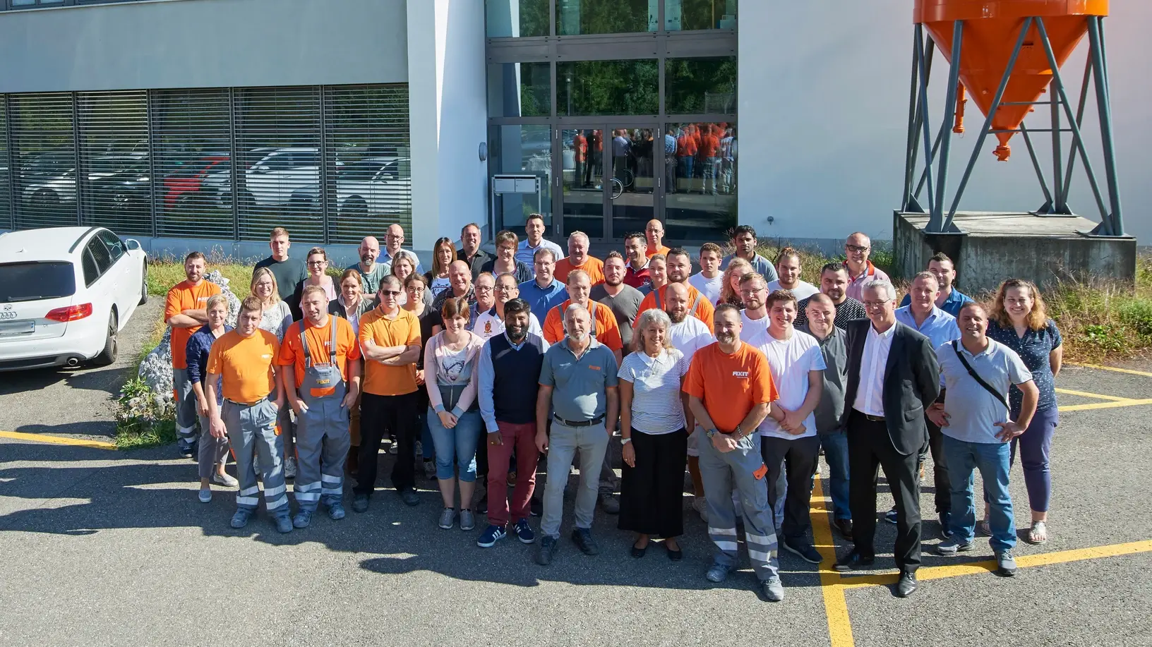 Fixit AG : photo de groupe de tous les collaborateurs sur le site de Holderbank AG devant le bâtiment administratif avec le silo Fixit