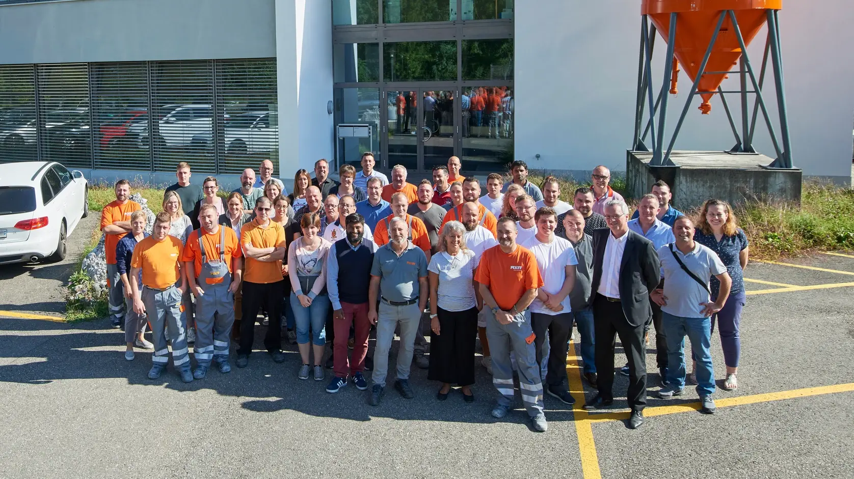 Fixit AG : photo de groupe de tous les collaborateurs sur le site de Holderbank AG devant le bâtiment administratif avec le silo Fixit