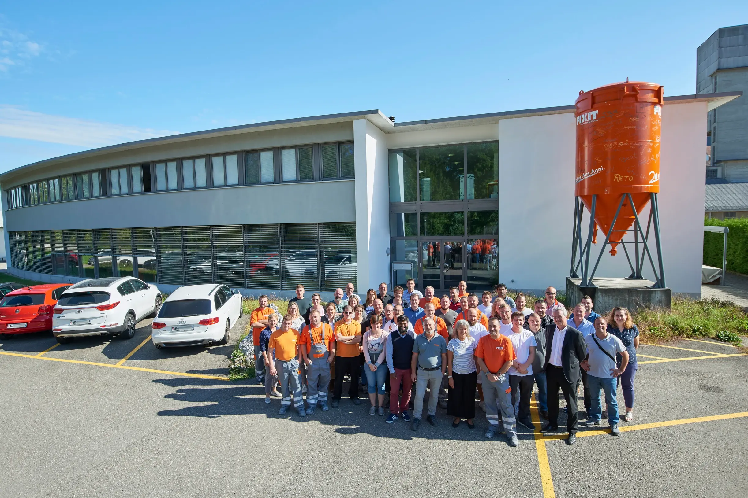 Fixit AG Photo de groupe de tous les collaborateurs du site de Holderbank AG devant le bâtiment administratif avec le silo Fixit.