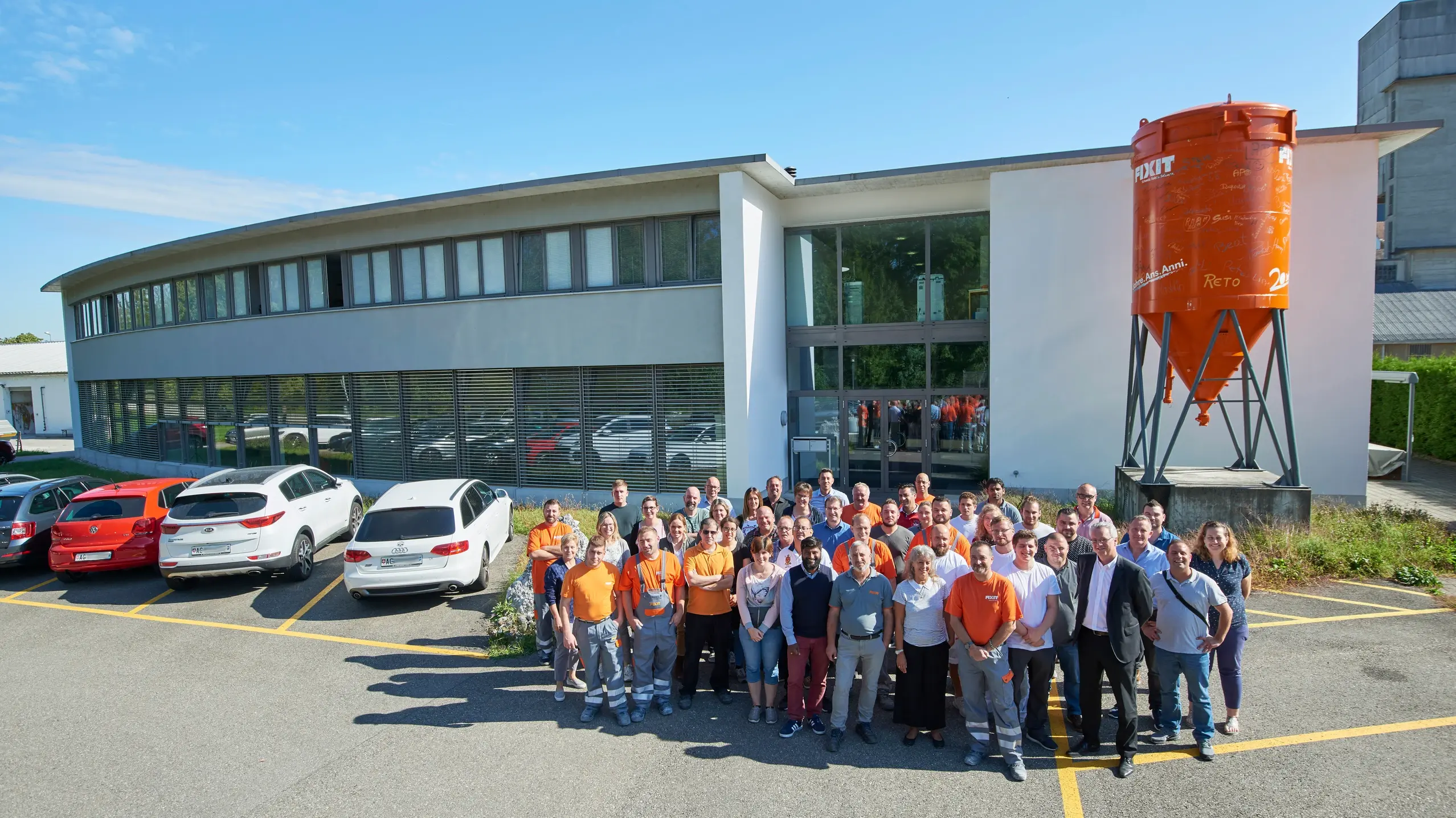 Fixit AG Gruppenfoto aller Mitarbeiter am Standort in Holderbank AG vor dem Verwaltungsgebäude mit Fixit Silo