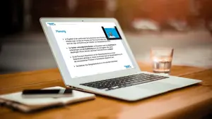 Schreibtisch mit einem Laptop, auf dem ein Webinar abgespielt wird