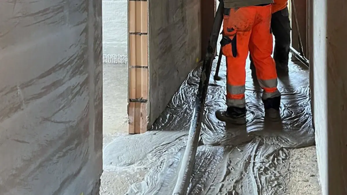 Detailansicht eines Hausflurs im Rohbauzustand mit einem Estrich-Schlauch, den Beinen eines Verarbeiters und flüssigem Fixit POR Schaummörtel auf dem Boden