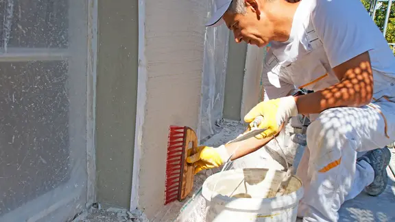 Mitarbeiter verstreicht den Putz an der Wand mit einem Besen