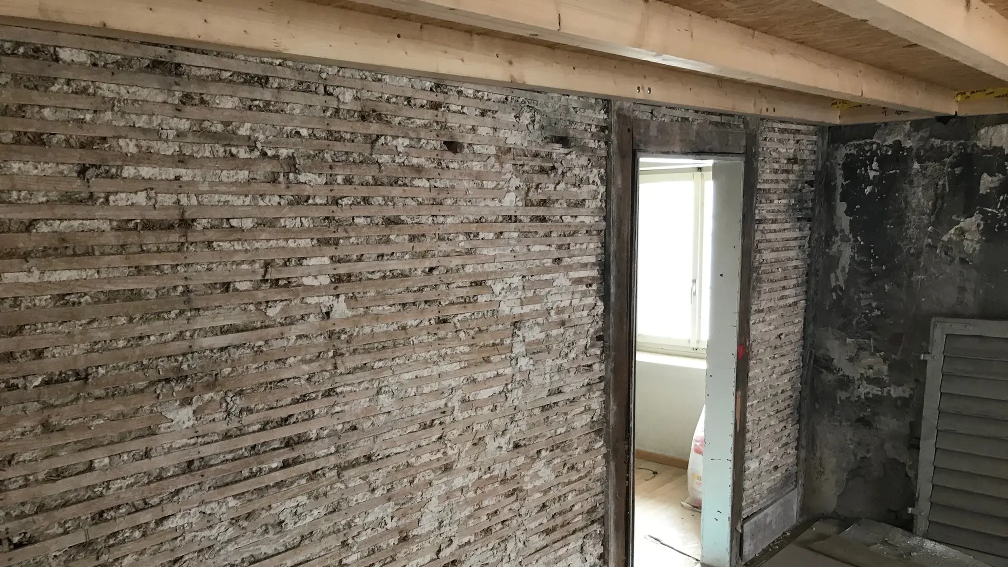 Alter Untergrund mit waagrechten Holzstäben in Lehm und einem Türdurchgang