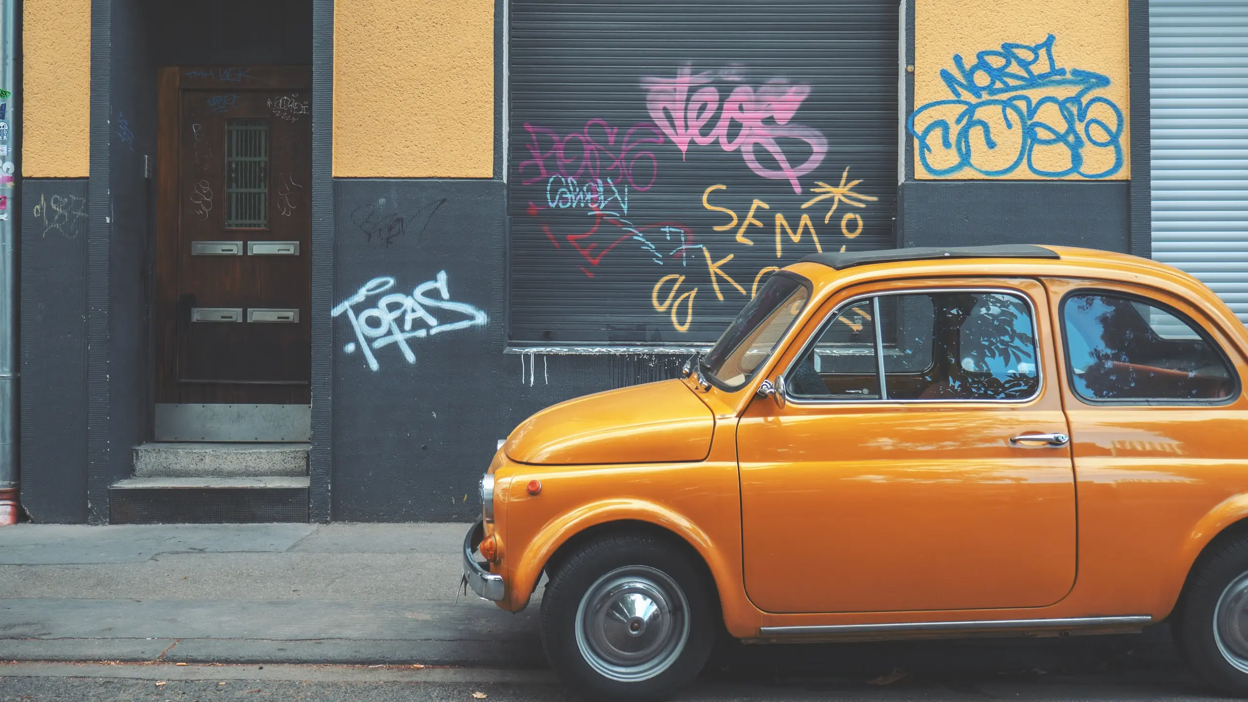 Eine mit Graffiti besprühte Fassade mit einem orangefarbenen Auto davor.