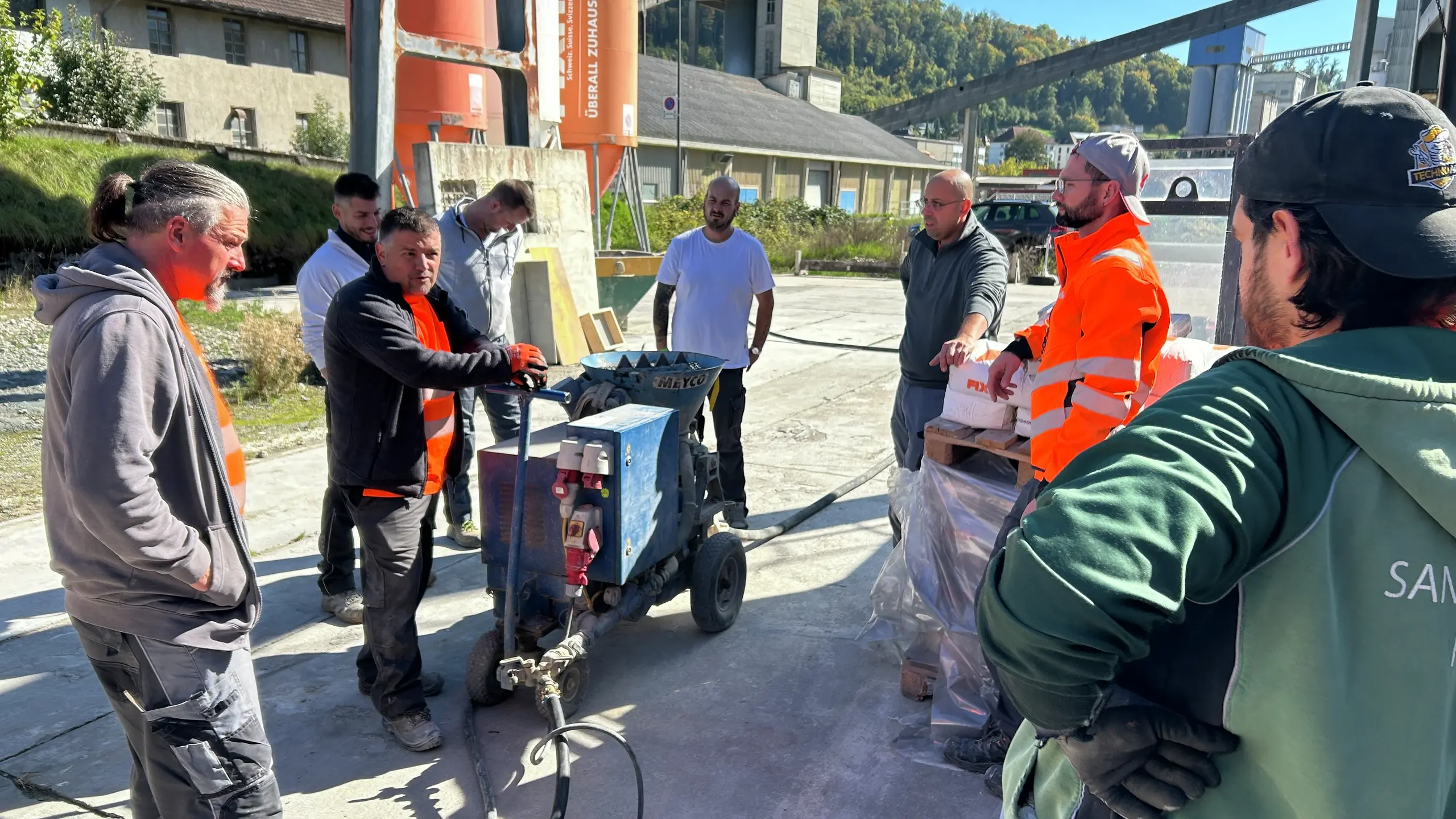 Remo Schwendener erklärt an einer Maschine deren Funktion, weitere Personen stehen im Kreis um das Gerät herum